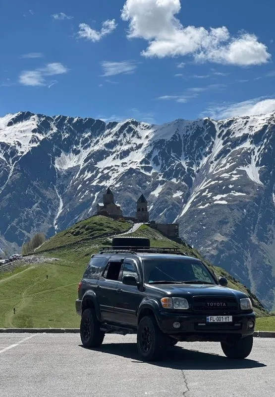 Black 4x4 parked on a mountain road below a snow-capped peak