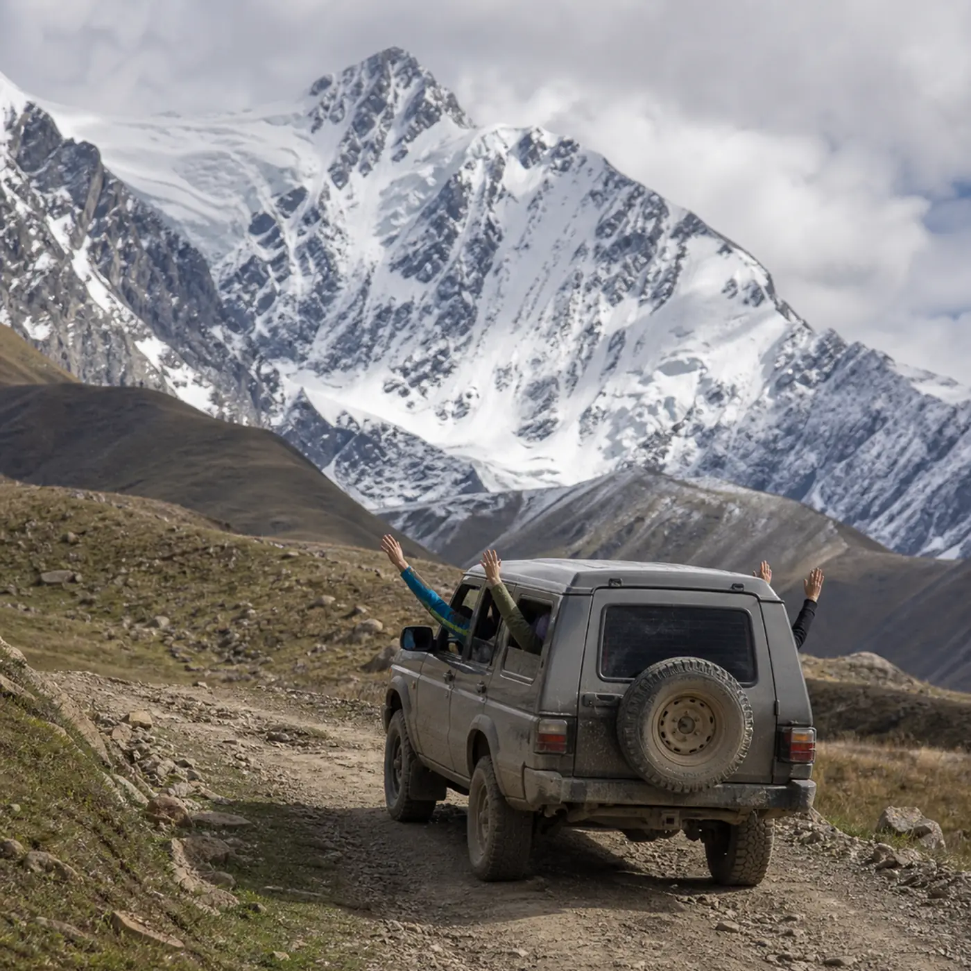 Travelers waving from a tour 4x4 below snowy peaks